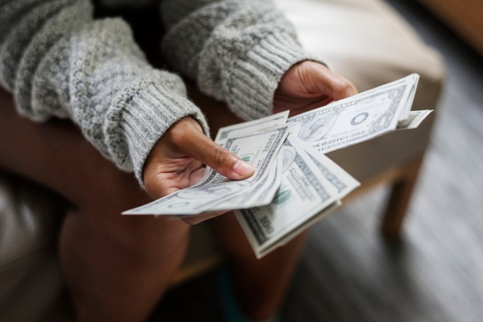 A woman's hands hold a set of fanned out of dollar bills. 